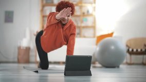 Cheerful active woman doing fitness at home, using tablet, watching online lessons on Internet. Positive well-fit lady in sportswear do plank exercises. Weight loss, muscle building. Health lifestyle.
