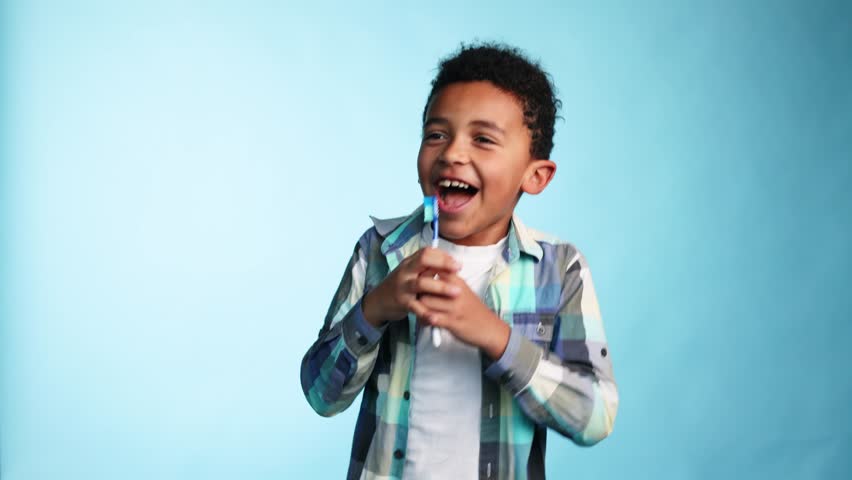 Cute little african american boy with teeth brush having fun and singing like with microphone on isolated blue background Adorable kid motivate other brushing teeth Daily healthcare concept | Shutterstock HD Video #1099440423