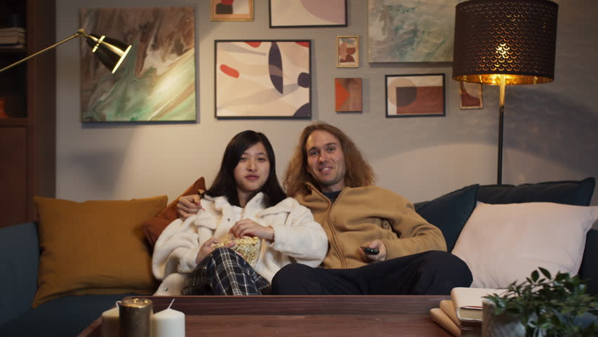 Beautiful young couple watching tv streaming platform cinema or sport show at home, mixed race family, diverse people and love, chinese woman and caucasian man, international friends on party | Shutterstock HD Video #1099443795