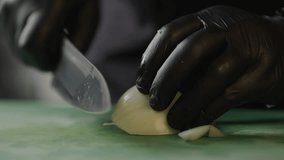 Slow motion close-up video of a chef cutting fresh onions with a knife on a cutting board. A professional prepares food in the kitchen of the restaurant.
