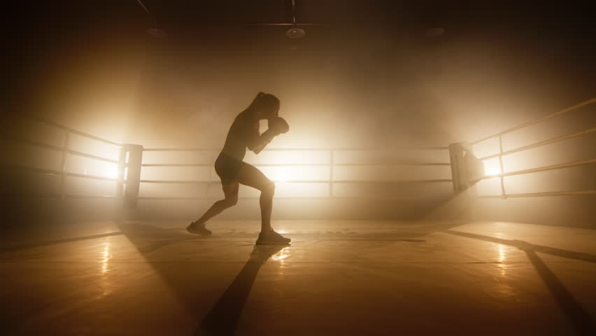 Silhouette of a confident, strong girl working out in gloves at gym studio. Close-up shot of active, female boxer punching and kicking in the air. High quality 4k footage in golden orange foggy light | Shutterstock HD Video #1099449971