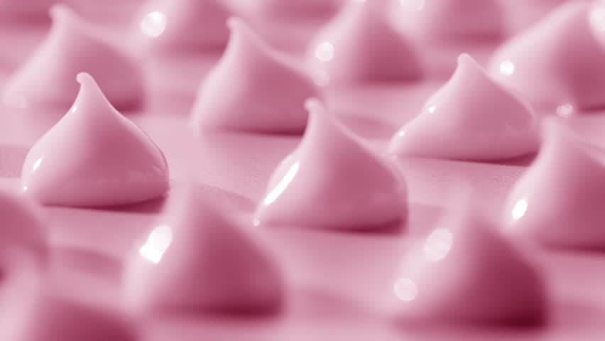 Macro crane shot of multiple drops of pink cosmetic cream with rose oil on pale pink background | Pink cosmetic cream commercial