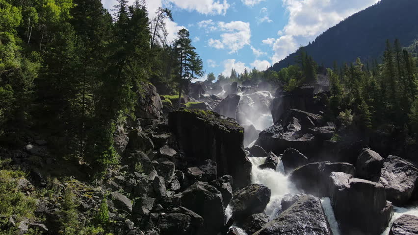 Aerial view of the cascading Uchar waterfall on the Chulcha River, flowing over rocks and pine forests. Beautiful wildlife in the Altai Mountains Royalty-Free Stock Footage #1099453213