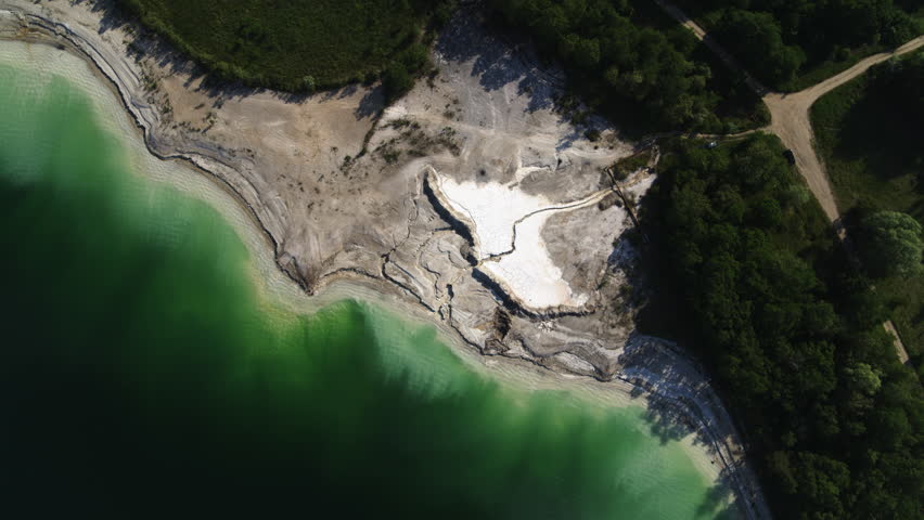 Aerial shot of limestone quarry green lake with clean dark green water and trees and sand