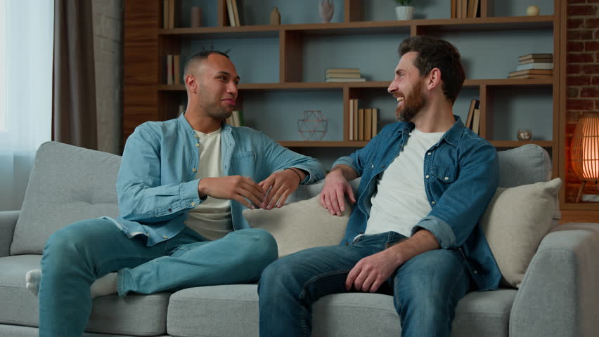 Two diverse 30s men businessmen talking at home on sofa multiracial friends companions african american caucasian ethnicity fellows brothers discussing plans friendly talk male dialogue conversation Royalty-Free Stock Footage #1099456551