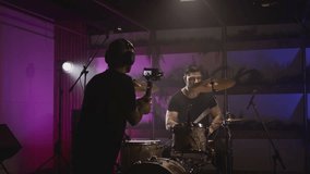 Shooting a music video. The director of photography makes a video, shoots a drummer musician. The view behind the scenes. Create a music video for a rock band. Creative director and crew.