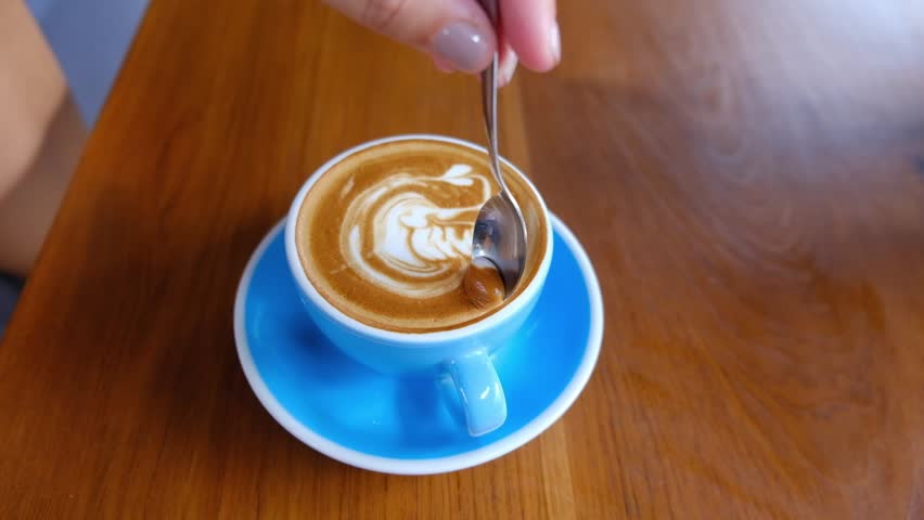 Woman mixing sugar in blue cup of cappuccino. Top view | Shutterstock HD Video #1099460157