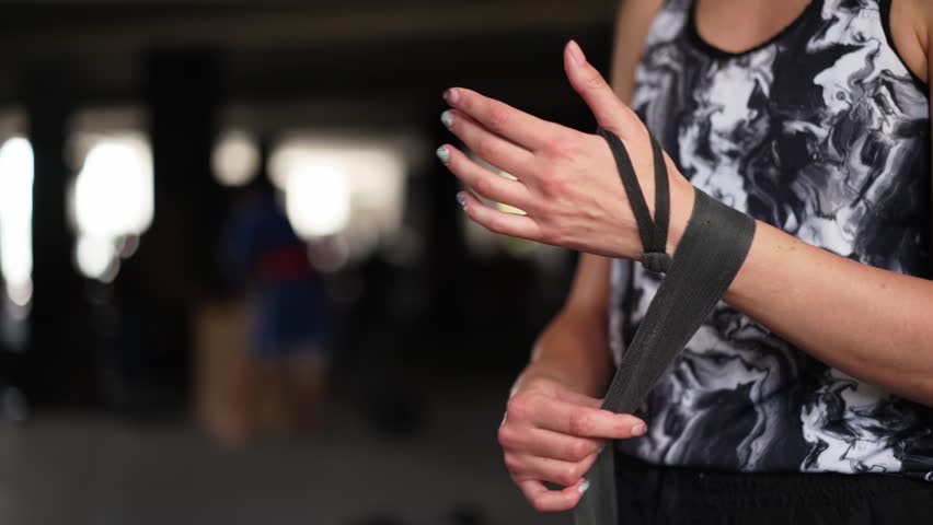 Athletic slim woman wrapping hands with boxing bandages at gym. Female athlete preparing for karate in fitness center. Sport, active lifestyle concept. Strong independent woman concept. Feminist