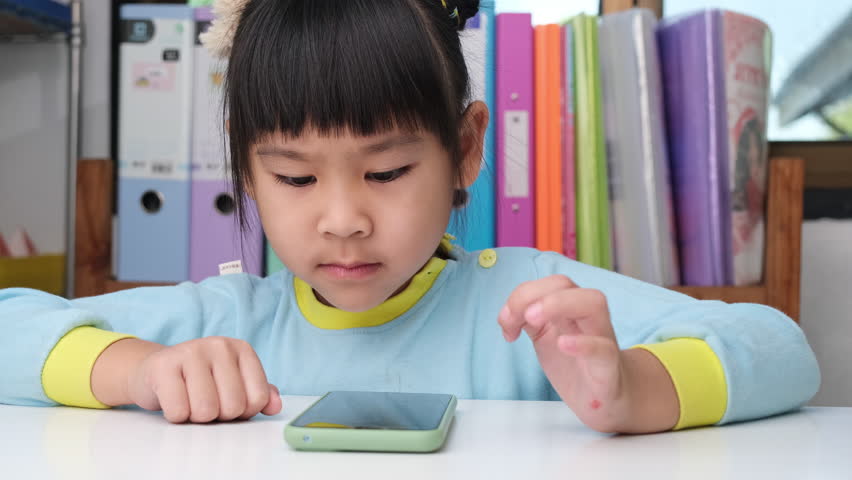 Cute little girl holding smartphone looking at screen smiling using application, playing online games, watching cartoons in living room at home. Children and modern technology concept | Shutterstock HD Video #1099462185