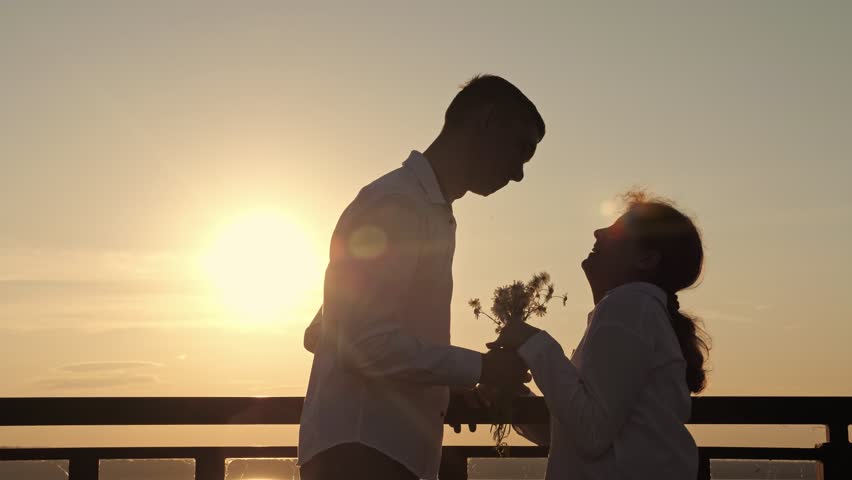 Young man with cerebral palsy gives present for woman against river. Male partner gives bouquet of flowers for woman at back sunset. Man shows love and appreciation | Shutterstock HD Video #1099463737