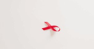 Vertical video of red hiv or aids awareness ribbon on white background with copy space. Health awareness, medical support and healthcare concept.