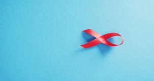 Vertical video of red hiv or aids awareness ribbon on blue background with copy space. Health awareness, medical support and healthcare concept.