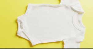 Vertical video of close up of white babygrow on yellow background with copy space. Baby, clothing, fabric, texture and materials concept.