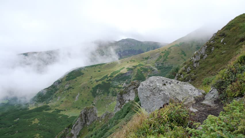 A man in blue sits on a rock and looks at the view from the top of the mountain. Portrait of a boy admiring nature in cloudy weather. Cumulonimbus. High quality 4k footage