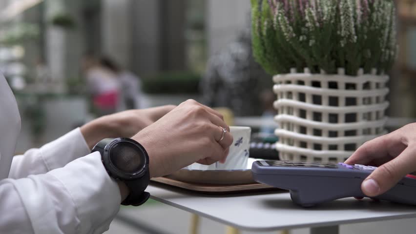 A woman pays a bill in a restaurant through a POS terminal using a smart watch. New NFC technology, cashless wallet, use of contactless convenient payment services. Royalty-Free Stock Footage #1099467565