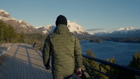A video showing the back view of a man walking at the observation deck, sightseeing the landscape of Nahuel Huapi park at Bariloche, Argentina during daytime