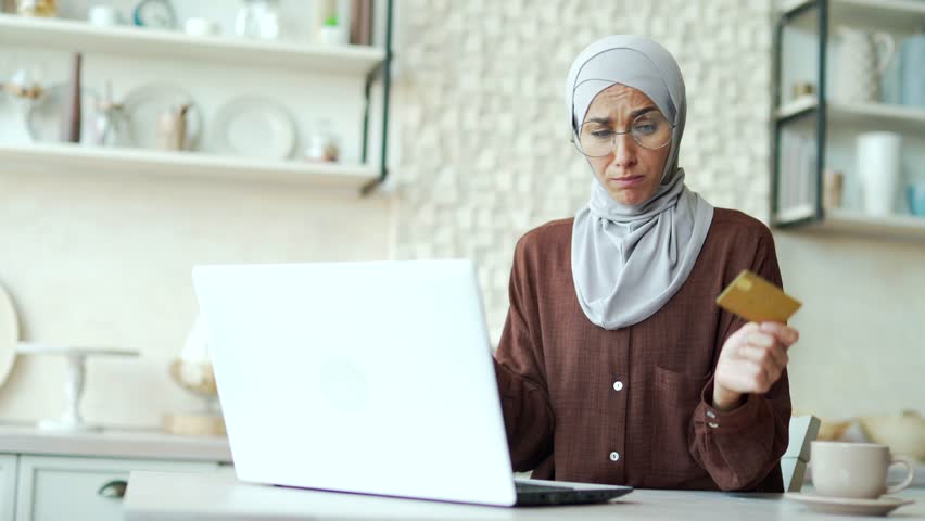 Confused young muslim woman in hijab with credit card having problem with online order payment error fraud or blocked bank account Stressed female doing shopping at internet money transfer withdrawal | Shutterstock HD Video #1099470067