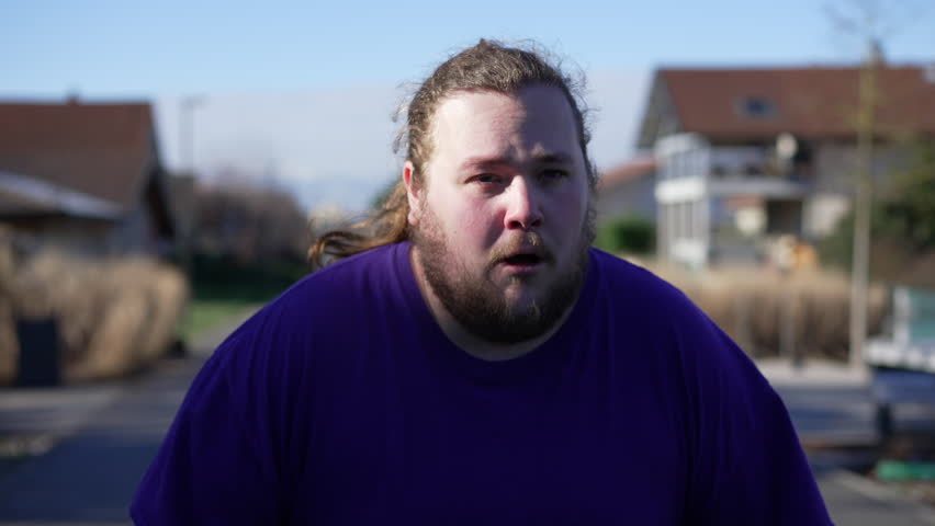 One exhausted overweight young man having chest pains standing outside. A fat male person having heart palpitations recovering breath standing outside | Shutterstock HD Video #1099470463