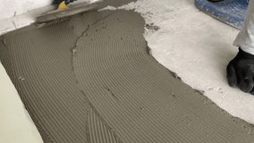 A builder applies tile adhesive to the floor. 4k video footage of construction work on laying tiles.