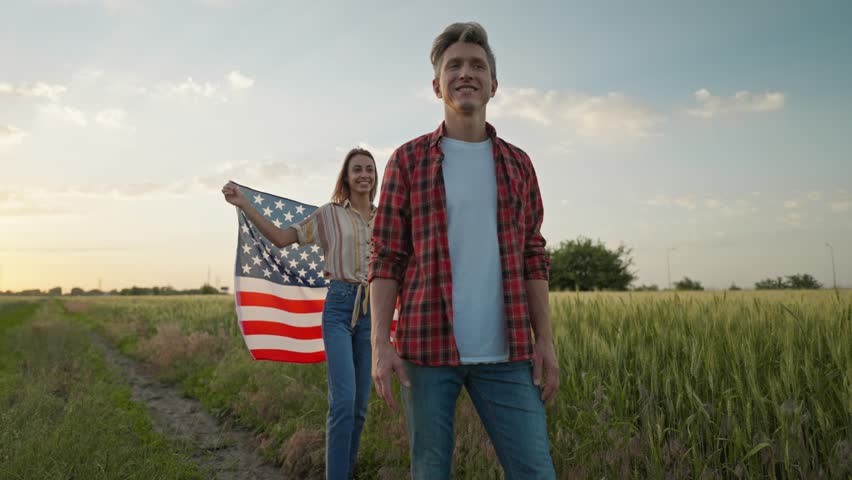 4k slow motion of happy patriotic couple celebrating fourth of july with national flag running in rural lardmark at sunset. 4th of July. USA independence day celebrating with American flag. Royalty-Free Stock Footage #1099475881