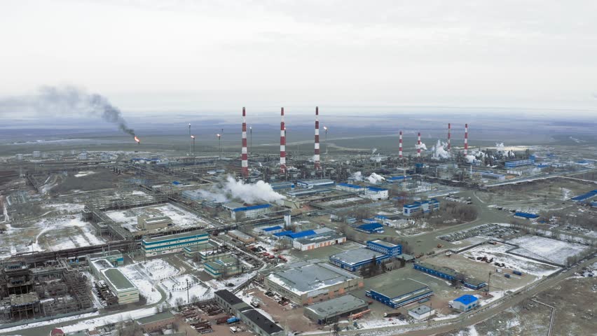 Drone landing with a view of a gas processing plant with smoking chimneys and a gas pipe running along the road during the cold season.