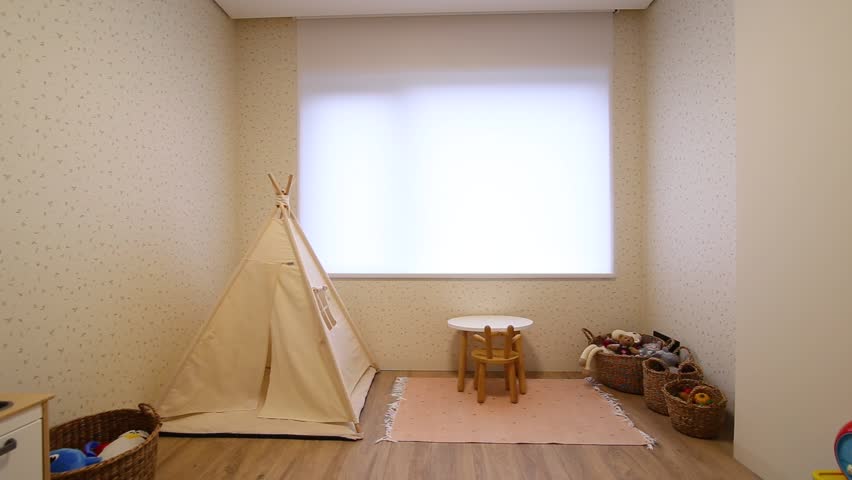 Motorized roller blinds in the children's room. Automatic roller shades on the window in the interior of child's room. Trees outside. Electric sunscreen curtains for home. Playhouse and toys there. Royalty-Free Stock Footage #1099479201