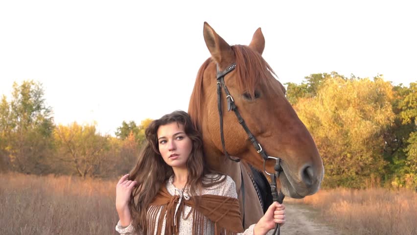 Slow Motion A young cowgirl woman stroking a horse in the sunset at her ranch. 