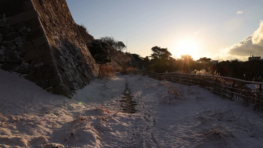 Slow pan over snowy pathway between stone wall and bamboo fence at sunrise