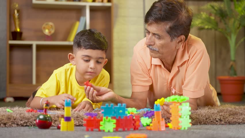 relaxed grandfather playing with grandson using toys on floor at home - concept of knowledge, retirement lifestyle and family bonding. Royalty-Free Stock Footage #1099480433