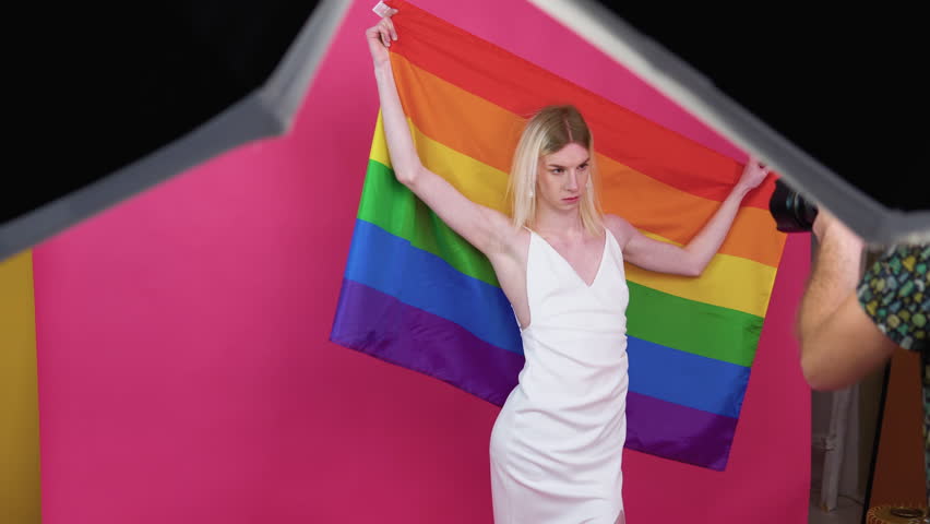 A photographer takes a photo to a young transgender man with rainbow flag