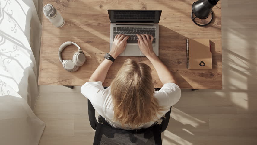 Girl at desktop, top down view, upset, disappointed, annoyed, takes her head with her hand. Emotional burnout at work or home office. freelancer can not do job and is tearing her hair out. | Shutterstock HD Video #1099486445
