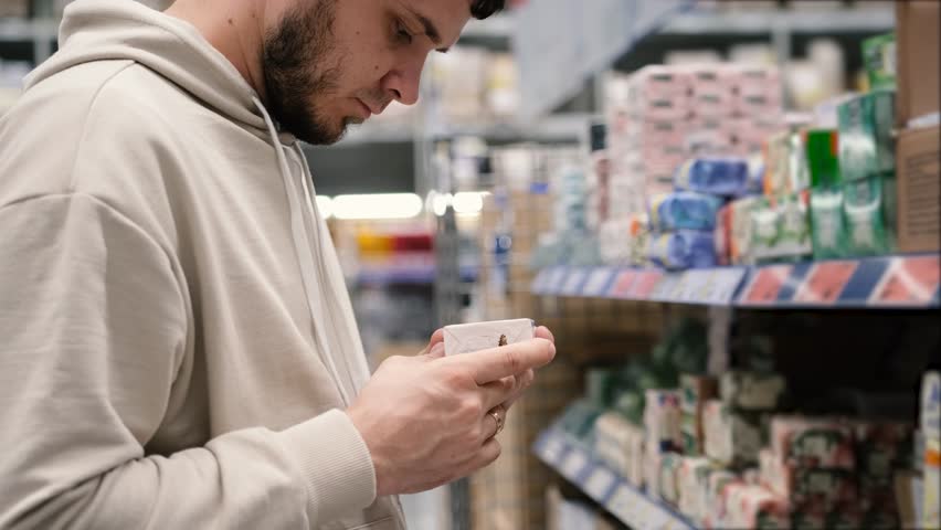 A man is shopping in the household goods section of a supermarket. A young man chooses soap in the store studies the composition | Shutterstock HD Video #1099486899