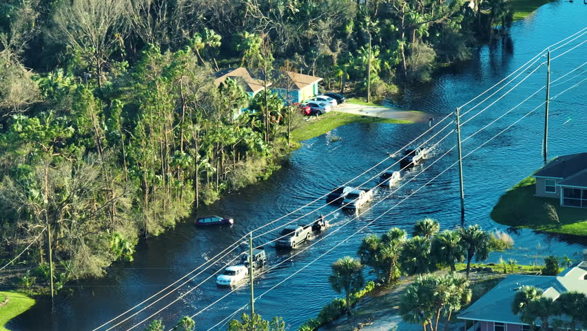 Flooded american street with moving vehicles and surrounded with water houses in Florida residential area. Consequences of hurricane Ian natural disaster