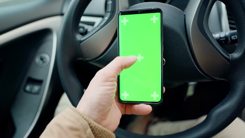 POV man in car at driver place, holds a phone with green screen with marks in hand. driver holds phone against steering wheel, swiping by finger in different directions. navigation, shopping concept | Shutterstock HD Video #1099492943
