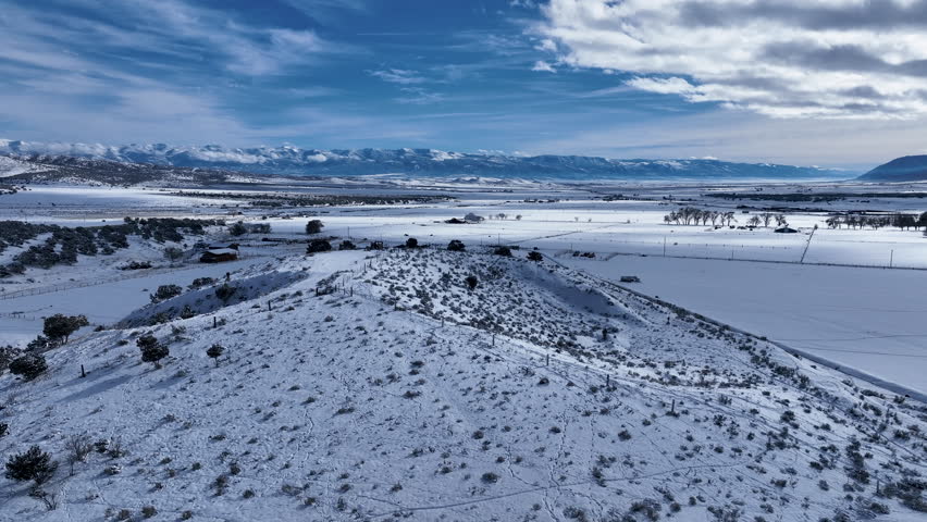 Aerial winter snow valley farm field barn hill 3. Aerial rural farming community agricultural economy. Homes and traffic on highway and Main Street. Mountain valley winter snow agriculture field.