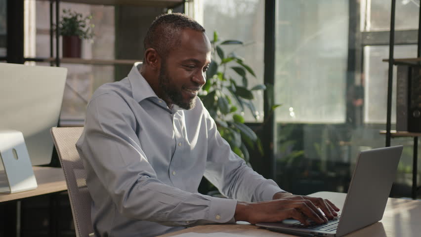 African American middle-aged senior mature businessman employee ethic 40s man singing song in office working online typing on laptop listen audio music having fun dancing funny dance celebrate victory | Shutterstock HD Video #1099498235