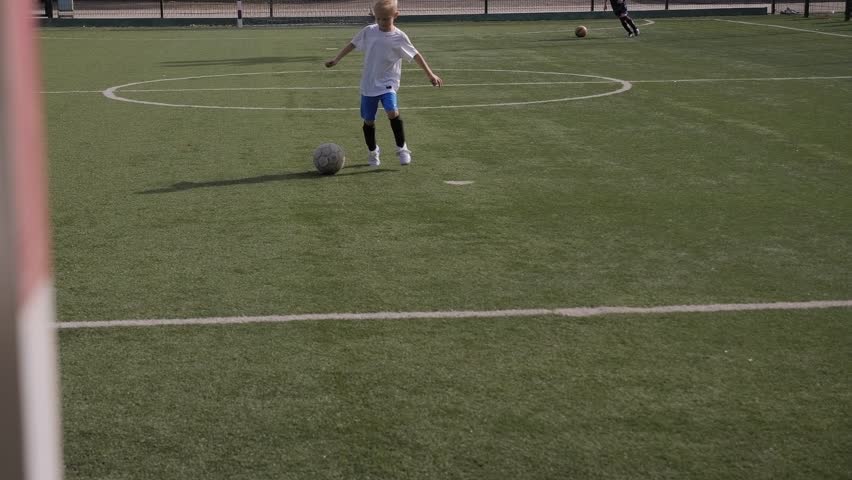 A little boy is playing soccer on the football field with an old torn ball, he hits the ball on goal. | Shutterstock HD Video #1099499993
