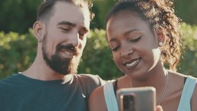 Close up, happy smiling couple watching video on mobile phone while sitting on bench