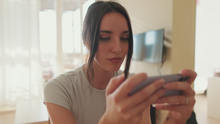 Young woman using mobile phone while sitting in apartment | Shutterstock HD Video #1099502939