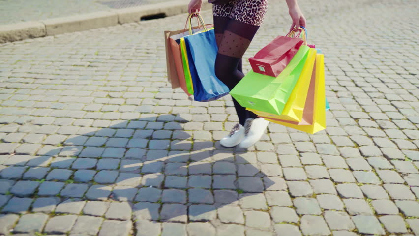 Trendy shopaholic woman with shopping bags walking on cobblestone across the city central street, satisfied shopper doing shopping and enjoying her perfect day, shopping at weekend. High quality 4k