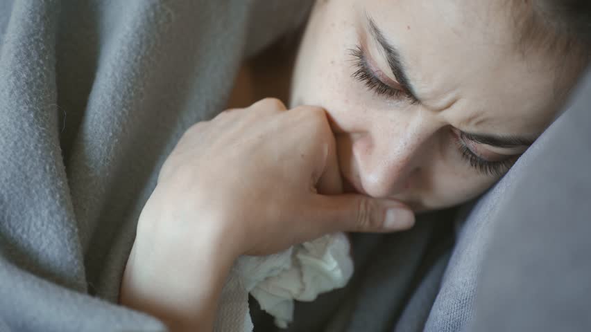 young woman lies alone on bed at home, cold and sick. illness, cold, virus, doctor's call at home, consultation with a doctor by phone