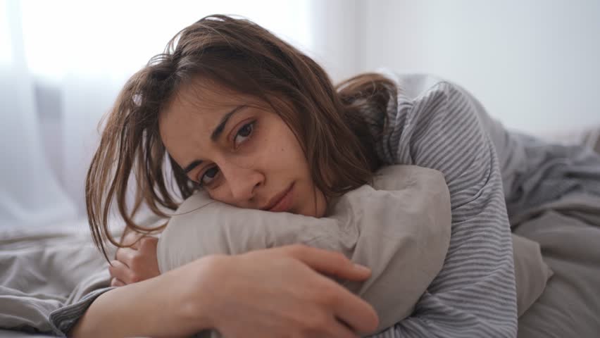 young woman lies alone on bed at home, cold and sick. illness, cold, virus, doctor's call at home, consultation with a doctor by phone