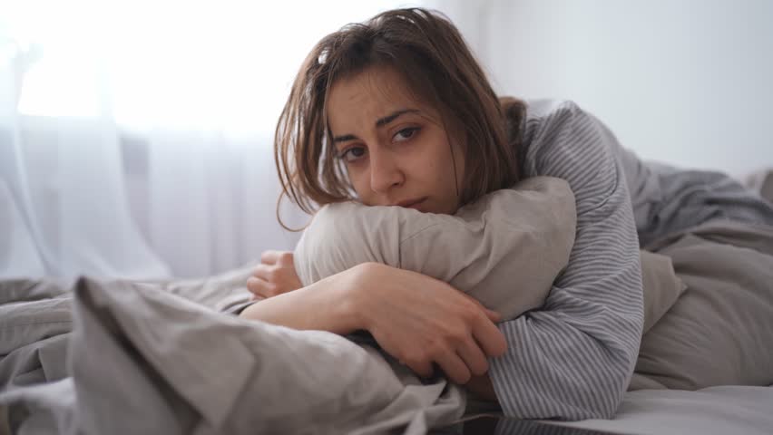 young woman lies alone on bed at home, cold and sick. illness, cold, virus, doctor's call at home, consultation with a doctor by phone