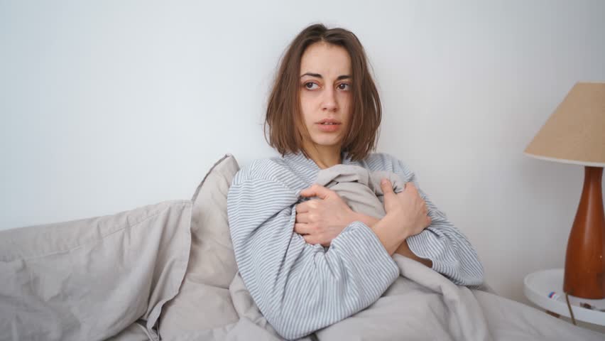 young woman lies alone on bed at home, cold and sick. illness, cold, virus, doctor's call at home, consultation with a doctor by phone