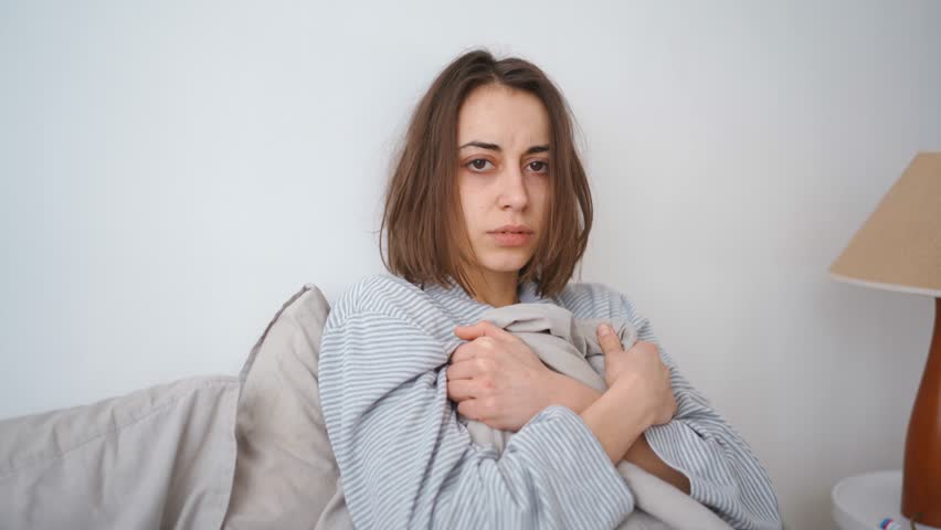 young woman lies alone on bed at home, cold and sick. illness, cold, virus, doctor's call at home, consultation with a doctor by phone