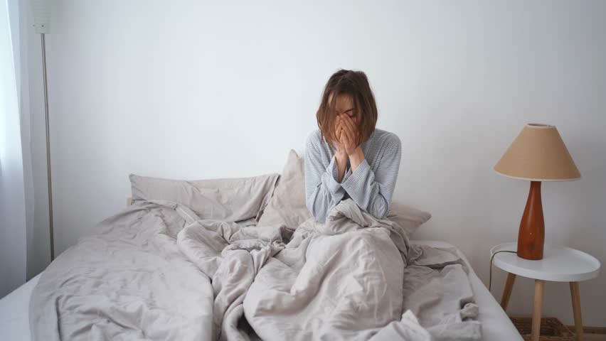 young woman lies alone on bed at home, cold and sick. illness, cold, virus, doctor's call at home, consultation with a doctor by phone