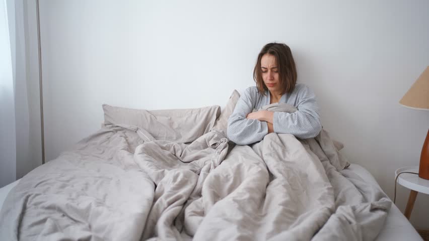 young woman lies alone on bed at home, cold and sick. illness, cold, virus, doctor's call at home, consultation with a doctor by phone