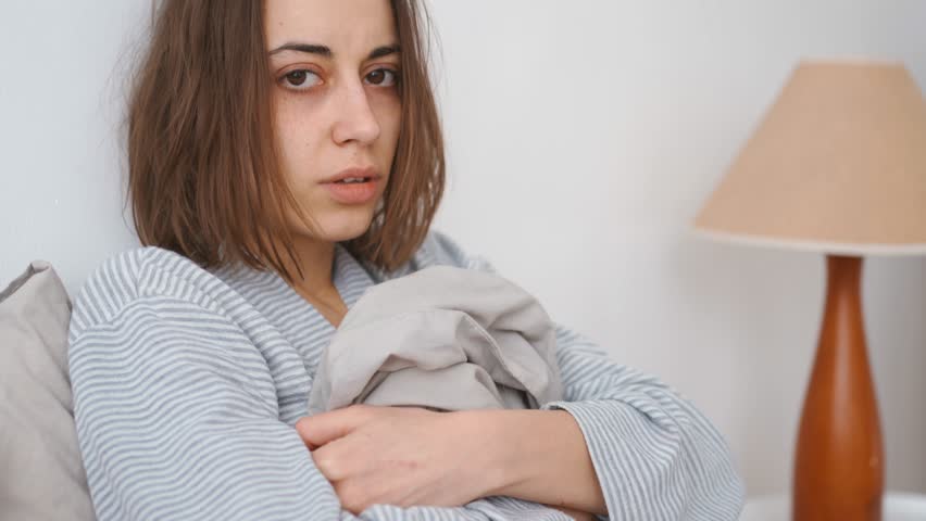 young woman lies alone on bed at home, cold and sick. illness, cold, virus, doctor's call at home, consultation with a doctor by phone