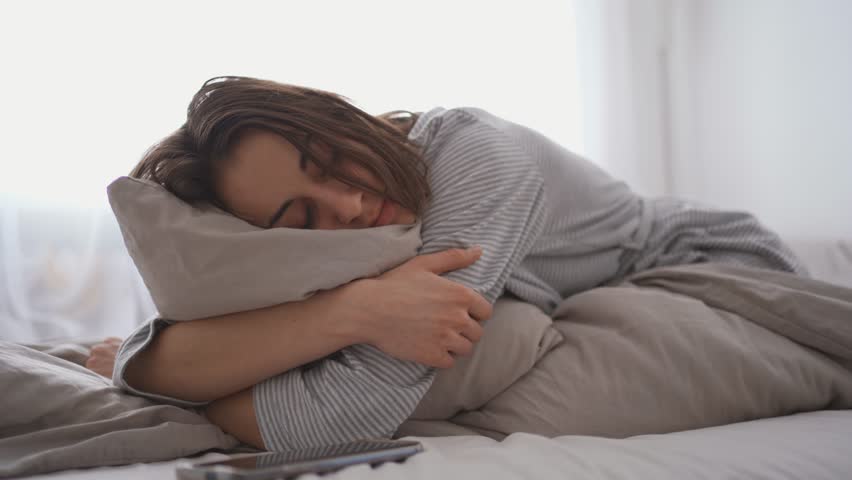 young woman lies alone on bed at home, cold and sick. illness, cold, virus, doctor's call at home, consultation with a doctor by phone