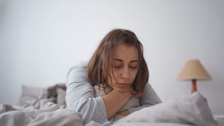 Young woman lies alone on bed at home, cold and sick. illness, cold, virus, doctor's call at home, consultation with a doctor by phone | Shutterstock HD Video #1099514049